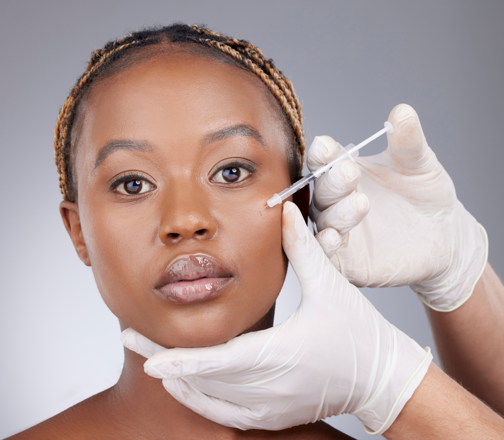 Woman, cheek and injection for beauty, collagen and treatment from aesthetic worker with hands. Black model, portrait and needle for dermal filler on white background in studio with hyaluronic acid